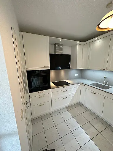 Elegante Häcker-Landhausküche mit Ravenna-Lackfronten in Weiß. Klassisches Rahmen-Design, Porzellan-/Messinggriffe, hochwertige Arbeitsplatte im Stein-Dekor. Inklusive Backofen auf ergonomischer Höhe, Spüleneinheit mit edler Armatur und viel Stauraum.
