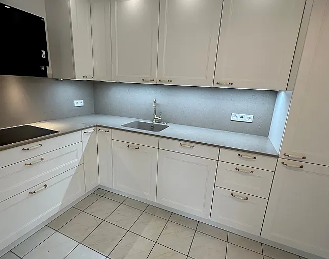 Elegante Häcker-Landhausküche mit Ravenna-Lackfronten in Weiß. Klassisches Rahmen-Design, Porzellan-/Messinggriffe, hochwertige Arbeitsplatte im Stein-Dekor. Inklusive Backofen auf ergonomischer Höhe, Spüleneinheit mit edler Armatur und viel Stauraum.
