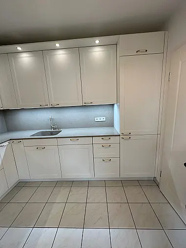 Elegante Häcker-Landhausküche mit Ravenna-Lackfronten in Weiß. Klassisches Rahmen-Design, Porzellan-/Messinggriffe, hochwertige Arbeitsplatte im Stein-Dekor. Inklusive Backofen auf ergonomischer Höhe, Spüleneinheit mit edler Armatur und viel Stauraum.