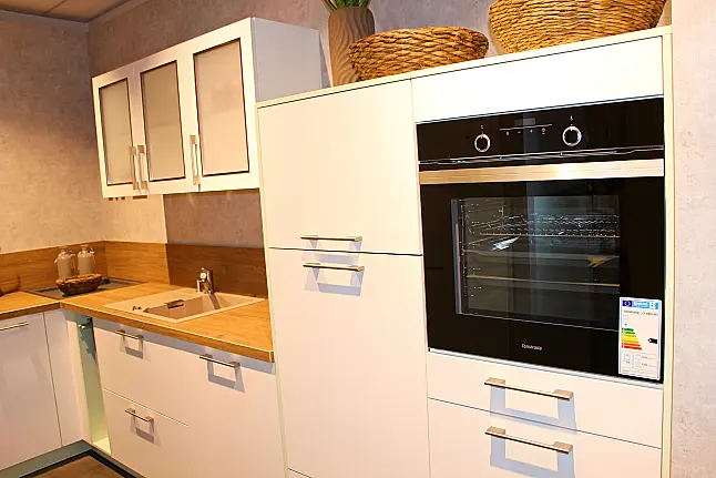Gemütliche L-Küche mit extra Geräte-Hochschrank für den Kühlschrank in moderner Kombination: Krsitallweiß matt, mit Massiver Steinplatte sowie Farbakzenten in Pastellgrün