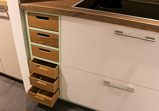 Gemütliche L-Küche mit extra Geräte-Hochschrank für den Kühlschrank in moderner Kombination: Krsitallweiß matt, mit Massiver Steinplatte sowie Farbakzenten in Pastellgrün