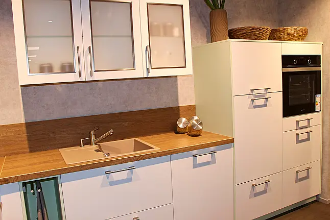Gemütliche L-Küche mit extra Geräte-Hochschrank für den Kühlschrank in moderner Kombination: Krsitallweiß matt, mit Massiver Steinplatte sowie Farbakzenten in Pastellgrün
