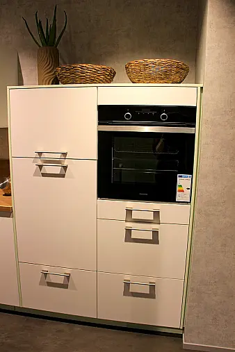 Gemütliche L-Küche mit extra Geräte-Hochschrank für den Kühlschrank in moderner Kombination: Krsitallweiß matt, mit Massiver Steinplatte sowie Farbakzenten in Pastellgrün