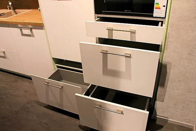 Gemütliche L-Küche mit extra Geräte-Hochschrank für den Kühlschrank in moderner Kombination: Krsitallweiß matt, mit Massiver Steinplatte sowie Farbakzenten in Pastellgrün