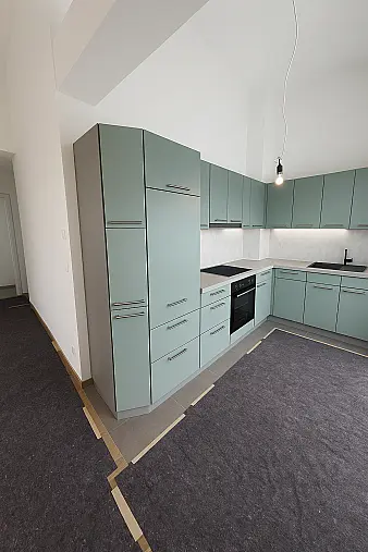 Zeitlos moderne L-Küche mit mattgrünen Fronten und klaren Linien. Die großzügige Arbeitsfläche in Steinoptik harmoniert perfekt mit den eleganten Edelstahlgriffen.