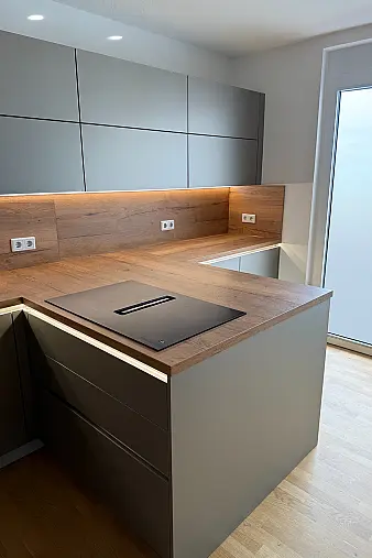 Moderne Designküche mit hochwertigen Polimerglas-Fronten in Sandgrau Metallic. Die warme Resopal-Arbeitsplatte in Alteiche Natur sorgt für einen edlen Kontrast und eine natürliche Ausstrahlung. Besondere Akzente setzt die elegante LED-Griffbeleuchtung.