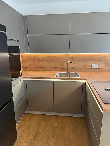 Moderne Designküche mit hochwertigen Polimerglas-Fronten in Sandgrau Metallic. Die warme Resopal-Arbeitsplatte in Alteiche Natur sorgt für einen edlen Kontrast und eine natürliche Ausstrahlung. Besondere Akzente setzt die elegante LED-Griffbeleuchtung.