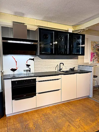 Elegante bauformat Küche „Potsdam“ in sandbeige Seidenmatt mit hochwertiger Granitarbeitsplatte und beleuchteten Glasoberschränken.