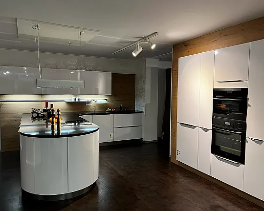 Sehr elegante gerundete, teilweise grifflose Küche mit Halbinsel in Hochglanz weiß mit schwarzer Steinplatte - Systemat Hochglanz weiß