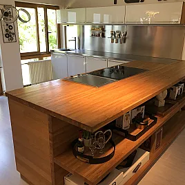 Naturholz trifft Glas. Schöne Küche mit Edelstahlarbeitsplatte, hochgebautem Backofen und Kochinsel