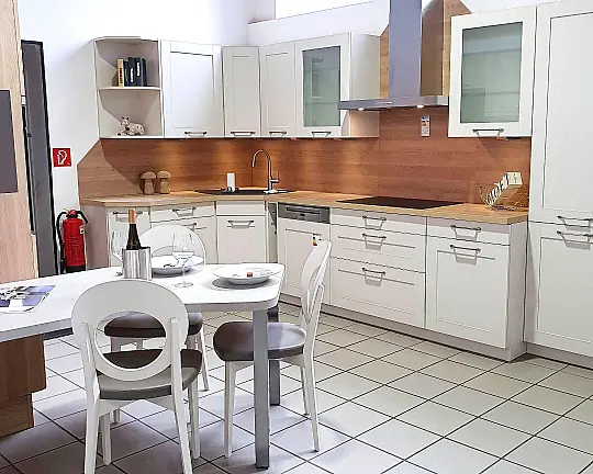 Müsterküche im modernen Landhaus-Stil für gemütliches Ambiente, raffinierte Tischlösung inklusive, L-Form mit Eckspüle und Hochschrankblock mit umbautem Standkühler. - Modell: FRAME, Farben: Magnolia mit Indian Oak,