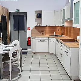 Müsterküche im modernen Landhaus-Stil für gemütliches Ambiente, raffinierte Tischlösung inklusive, L-Form mit Eckspüle und Hochschrankblock mit umbautem Standkühler.